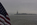 A moody New York Harbor scene featuring a patriotic view of Liberty Island and the Statue of Liberty partially obscured in dense fog, New York City